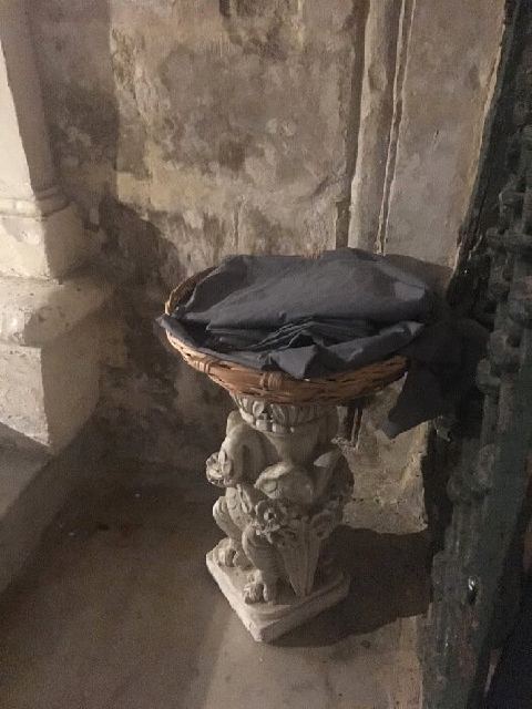 A basket on a stone stand containing shawls to cover up skin in St. Paul’s grotto.