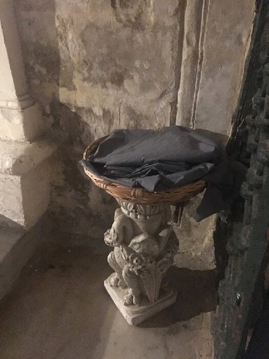 A basket on a stone stand containing shawls to cover up skin in St. Paul's grotto.