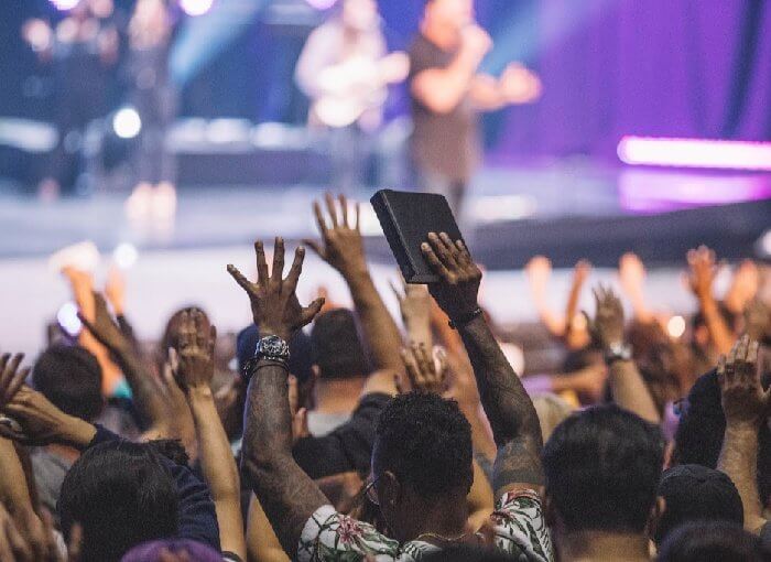 A crowded Protestant worship service with people lifting their hands in the air.